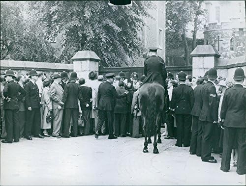 Гроздобер фотографија на група луѓе, опкружена од полицајци пред портата на зградата.